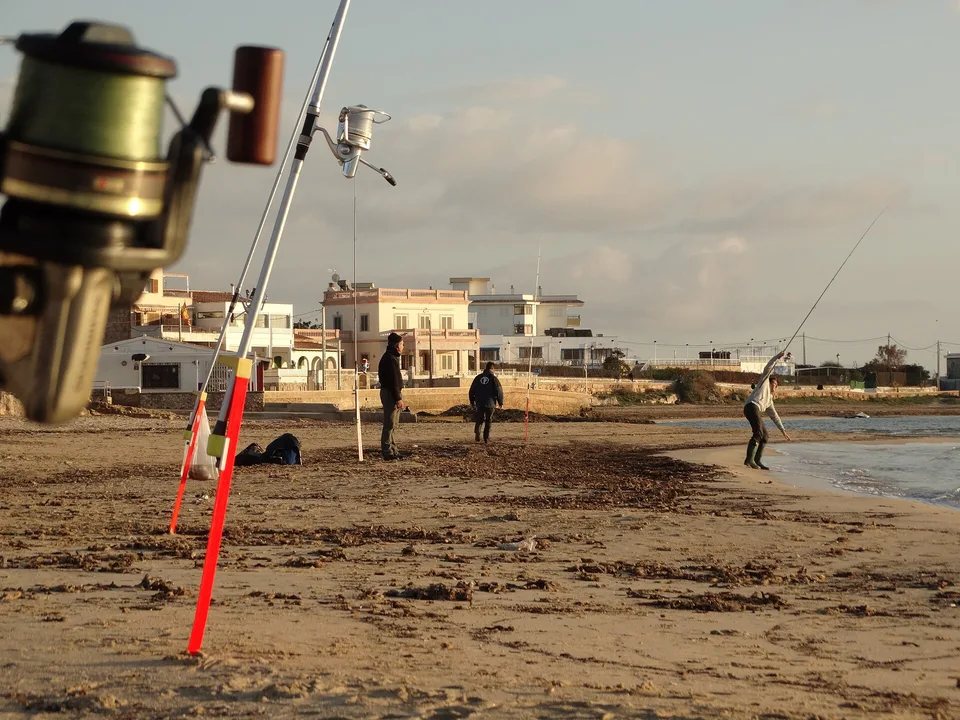 Pescador lanzando desde la playa con varias cañas montadas en primer plano