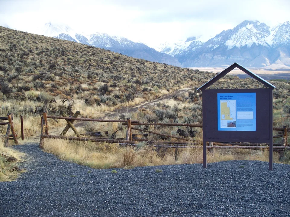 Panel informativo y acceso señalizado a un río de pesca entre montañas