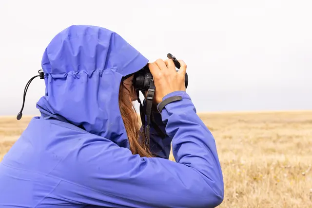 Persona con chubasquero observa con prismáticos una llanura