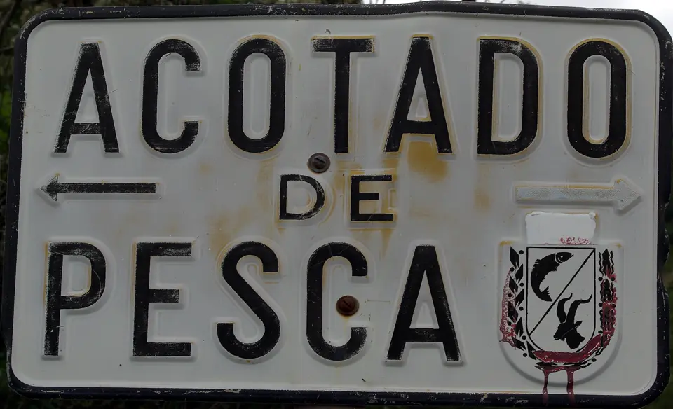 Señal metálica antigua con el texto «Acotado de pesca», flechas y un escudo