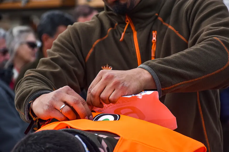 Manos que ajustan un chaleco naranja de alta visibilidad sobre un forro polar