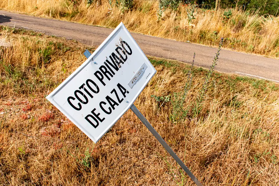 Cartel de «Coto privado de caza» inclinado entre hierba seca junto a un camino