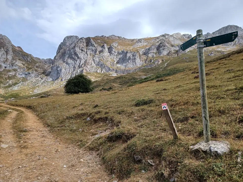 Camino de tierra con un poste indicador de madera en un valle de montaña bajo el cielo nublado